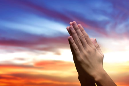 Human hands raised while praying to god with a sunset sky background